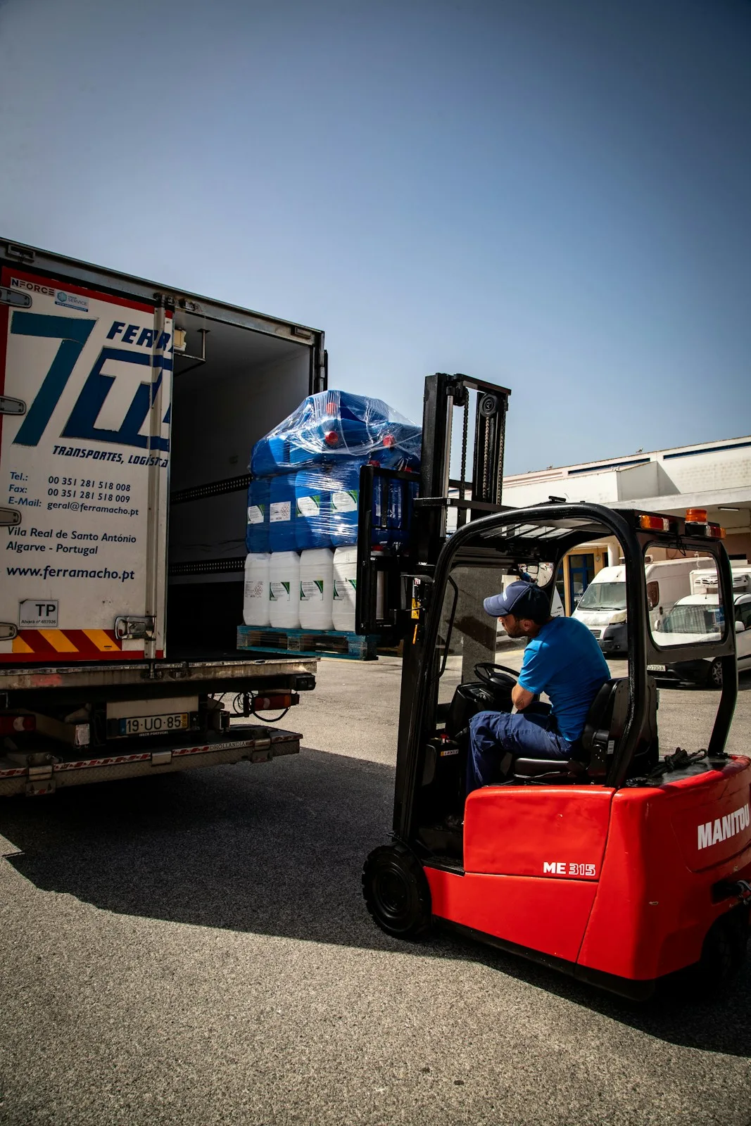 A forklift loading a stretch-wrapped pallet of containers into the back of a truck