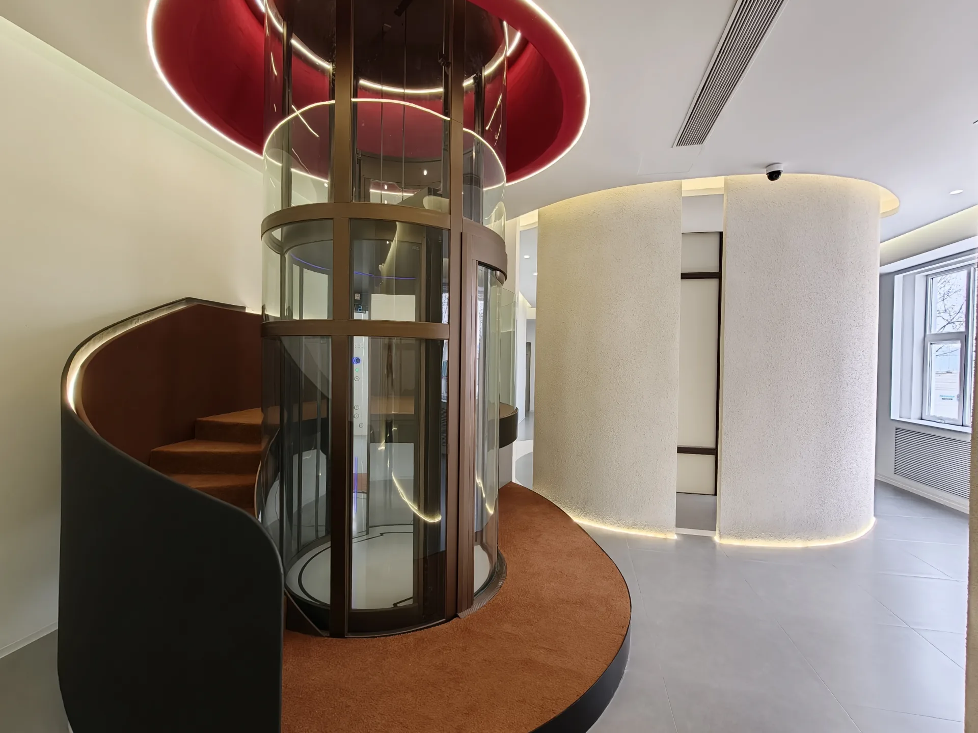 Round glass elevator beside a curved staircase in the Beijing showroom