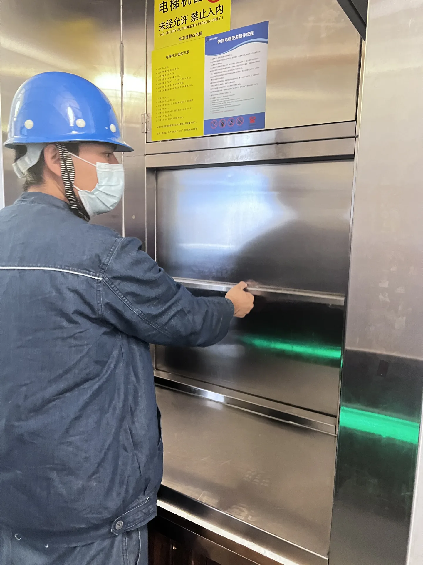 Technician checking the vertical sliding door of a stainless steel dumbwaiter