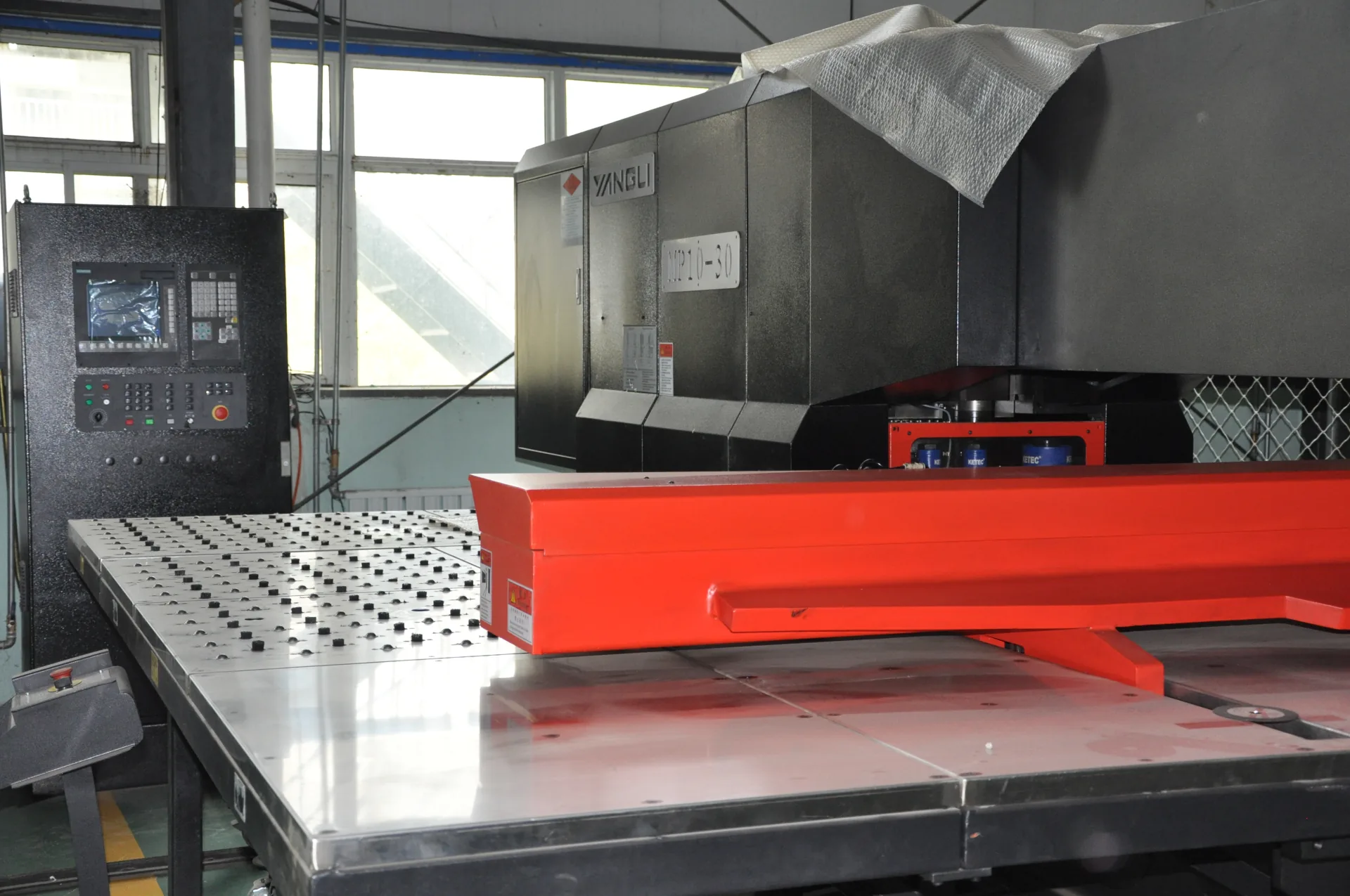 A CNC turret punch press and sheet-metal worktable inside a workshop.