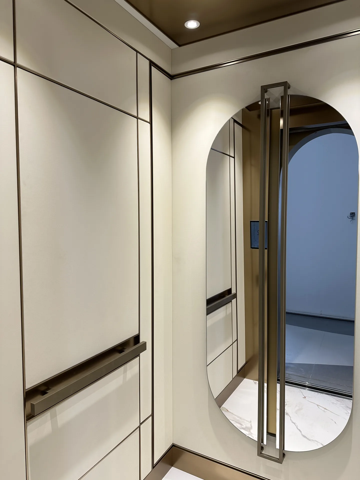 Cream elevator cabin panels with metallic trim, a handrail and an oval mirror