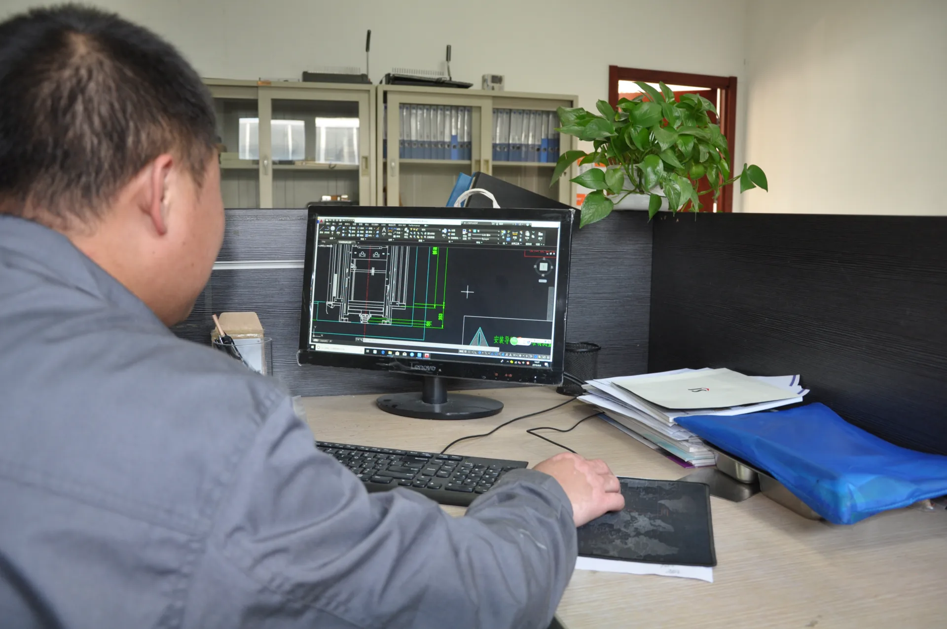 An engineer reviewing a lift CAD drawing at a workstation.