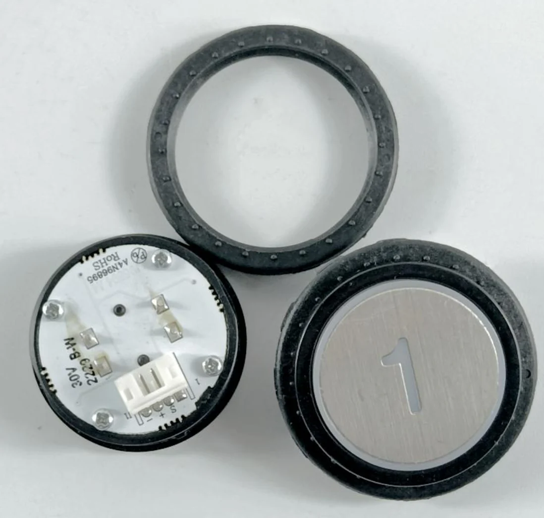 Front and rear of a round floor button with its retaining ring