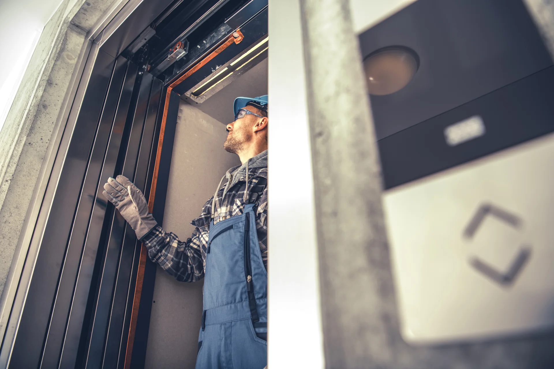 Technician inspecting the upper mechanism of an elevator doorway