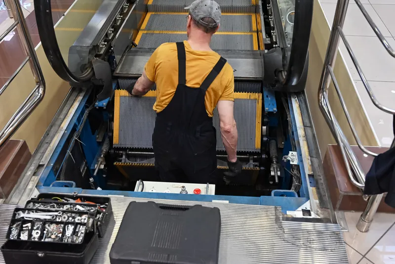 Technician working on an exposed mechanism beneath escalator steps