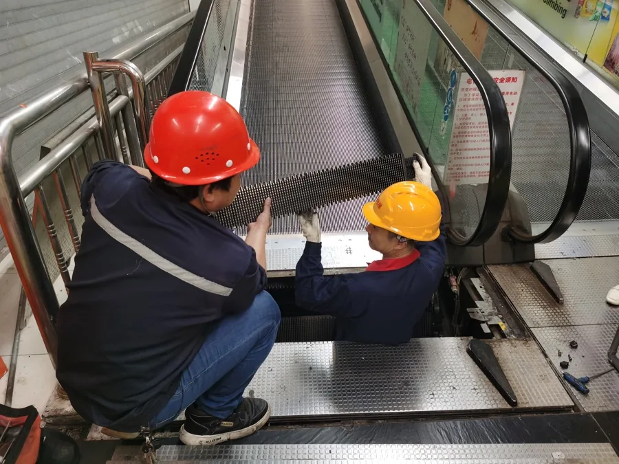 Two technicians lifting a pallet from an open moving-walk entrance section