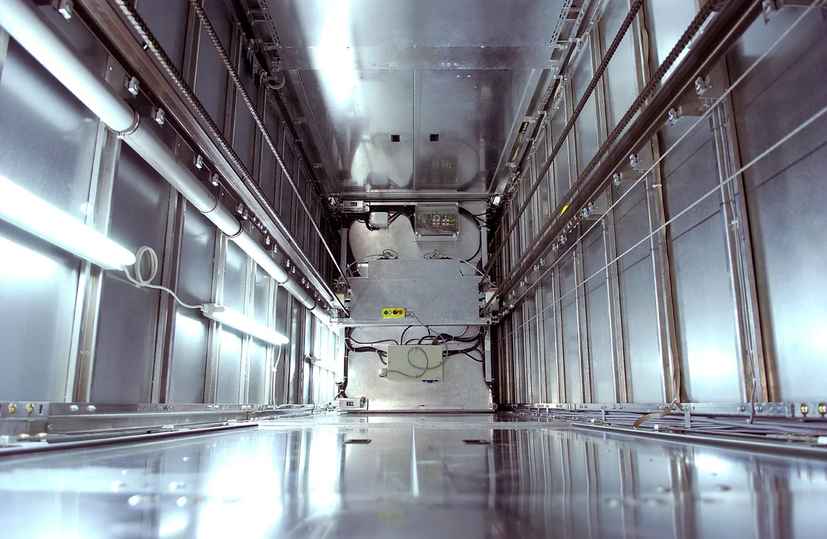 Interior of a metal-clad lift shaft showing guides, chains and lighting