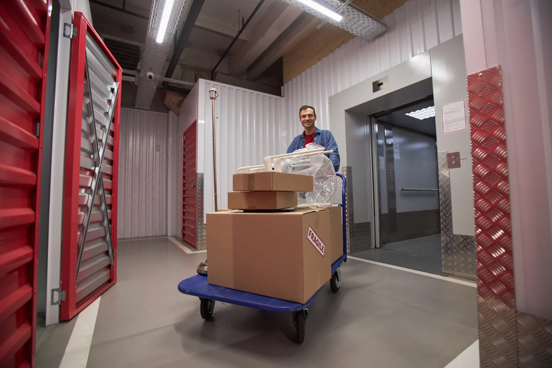 Worker moving a cart of boxes beside an open freight elevator
