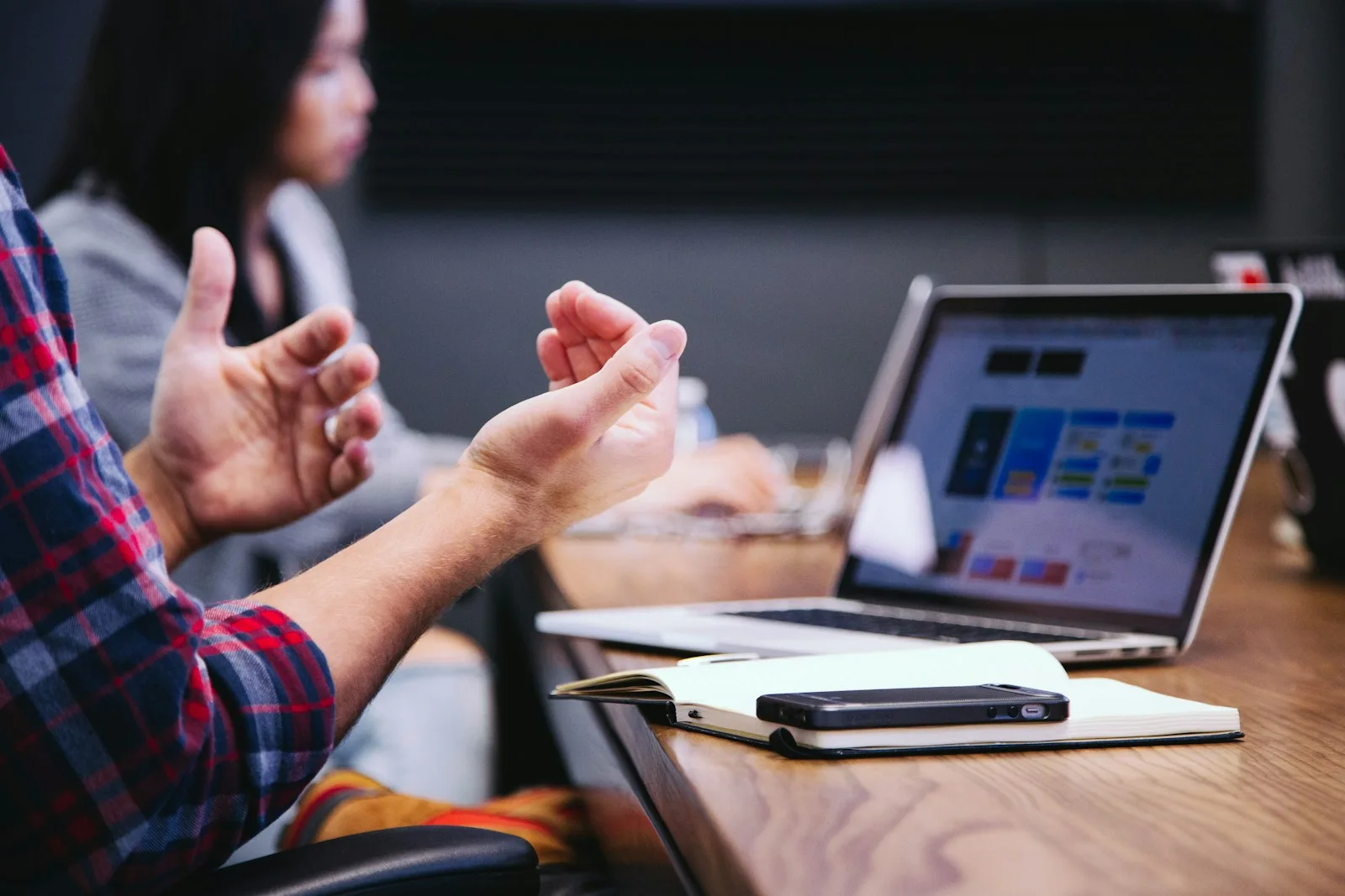Hands gesturing in a discussion beside a laptop, open notebook and phone