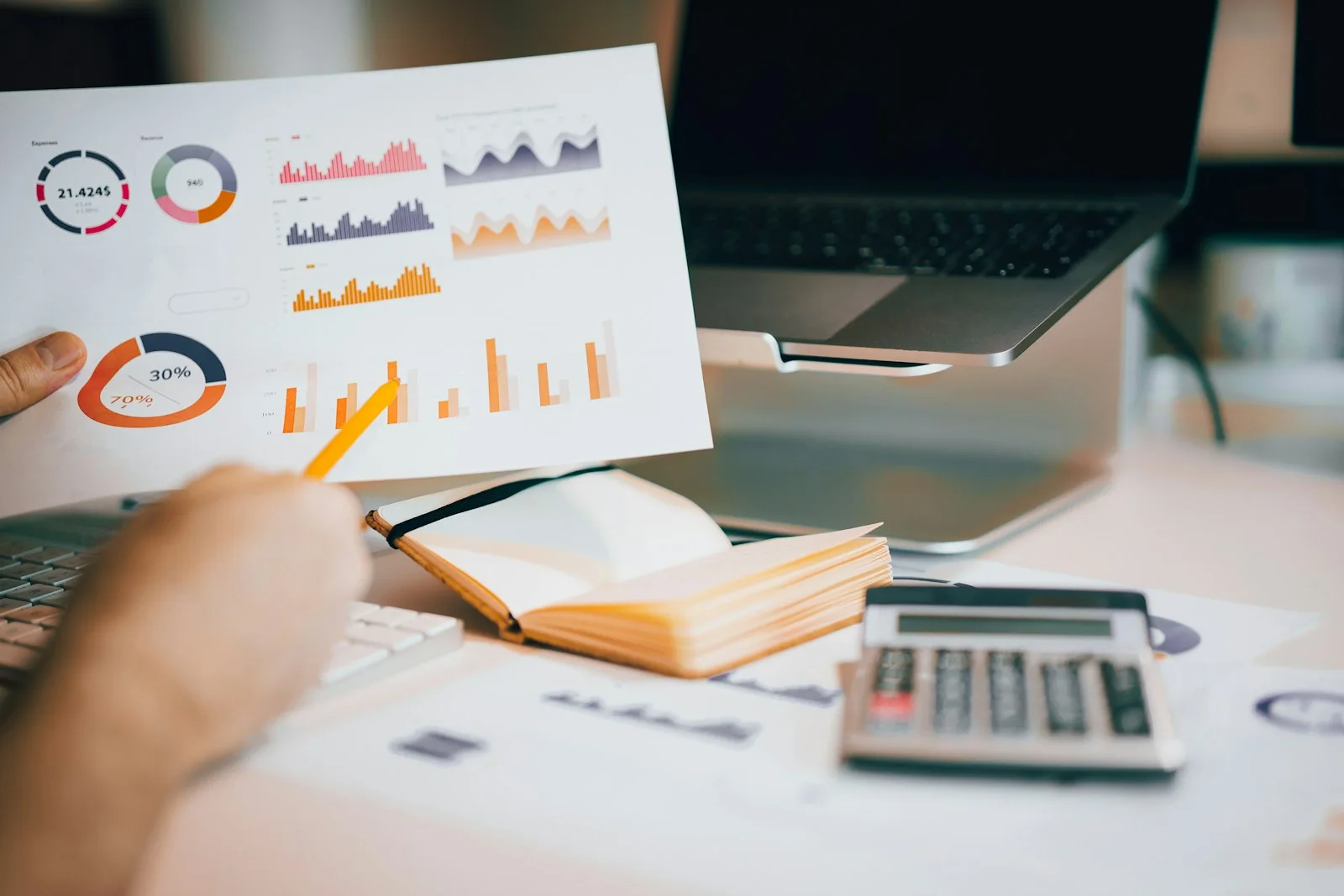 Hands reviewing printed charts beside a laptop, notebook and calculator