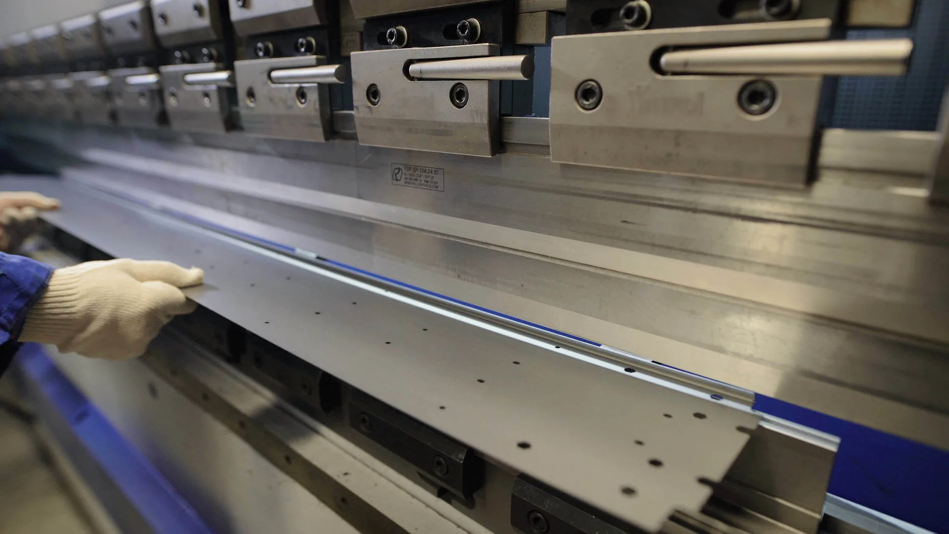 A gloved operator positioning a perforated sheet-metal panel at a press brake.