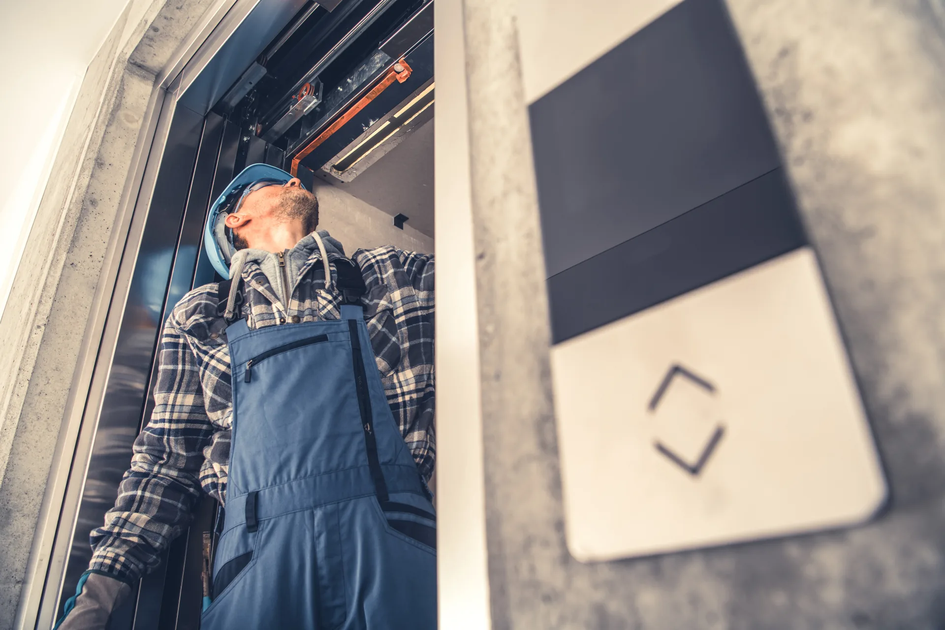 Maintenance technician examining equipment above an open elevator landing entrance