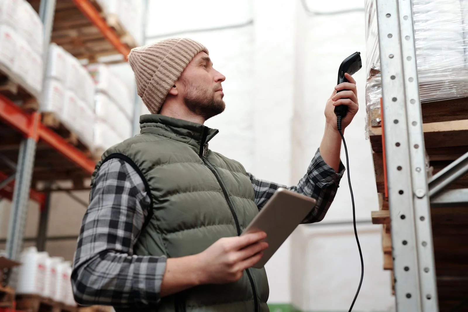 A warehouse worker using a handheld scanner and tablet beside pallet racking