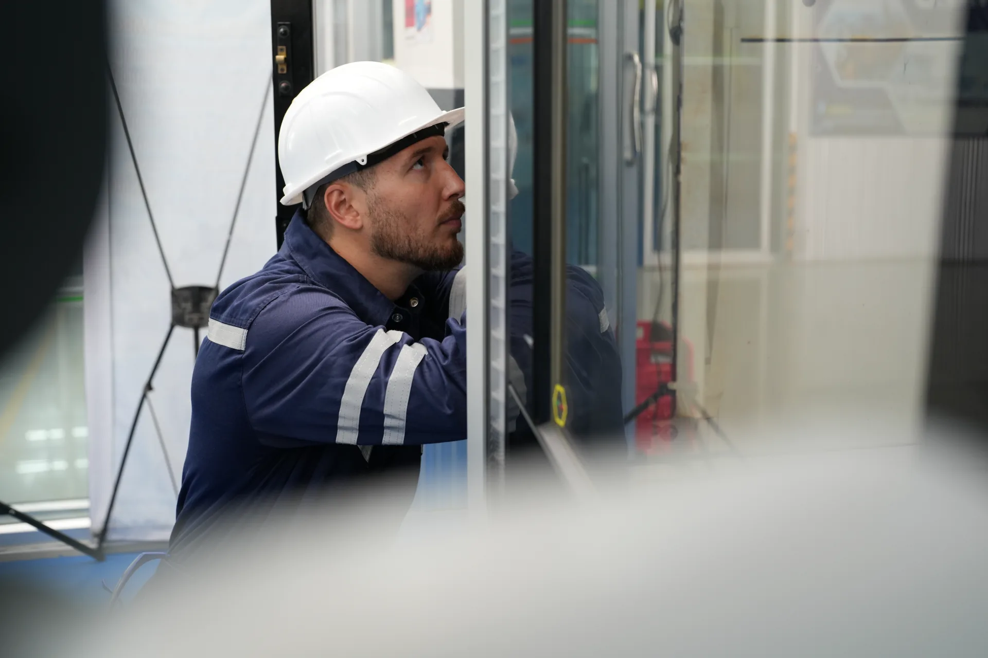 Technician wearing a hard hat inspecting a glass elevator panel