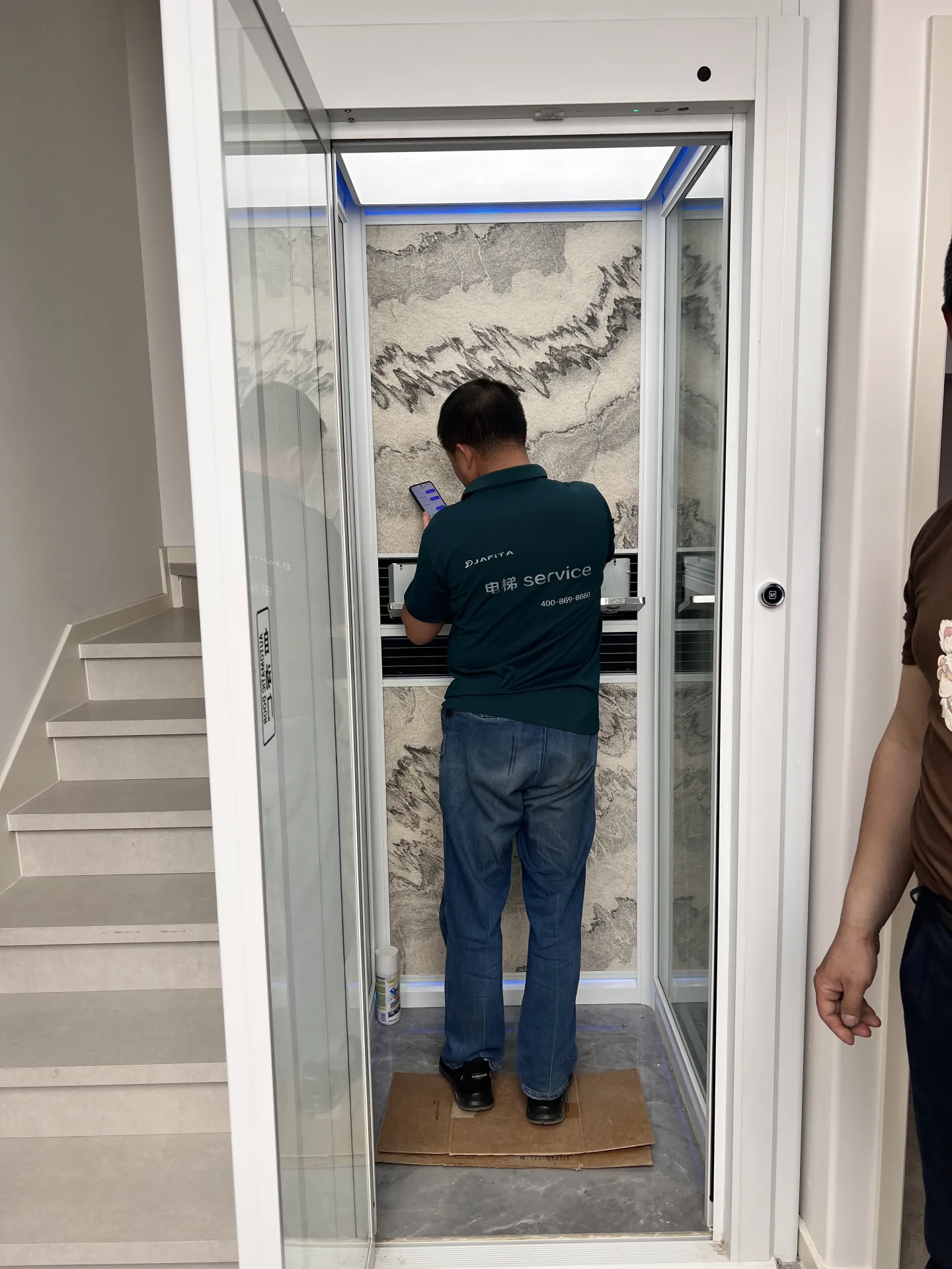JAFITA service technician working inside a home elevator with a glass swing door